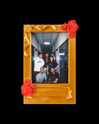 Gold-toned photo frame with red rose accents holding a vertical group photo on a black background