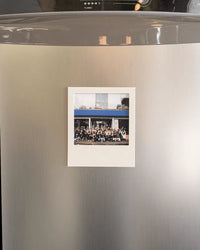 Small white photo frame displayed on a stainless steel refrigerator door