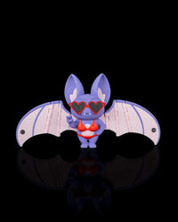 Purple bat figurine with pink wings, red swimwear, and heart-shaped sunglasses on a black background