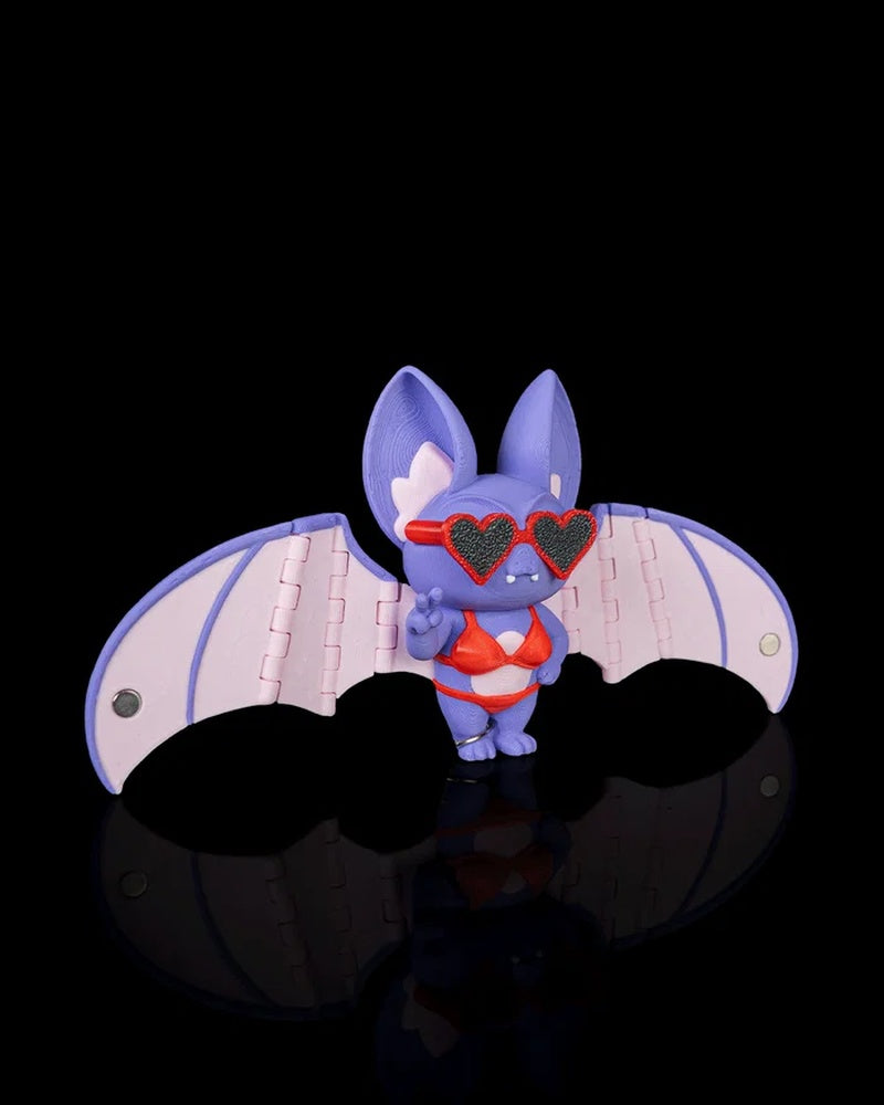 Purple bat figurine angled to the side with pink wings and heart-shaped sunglasses on a black background