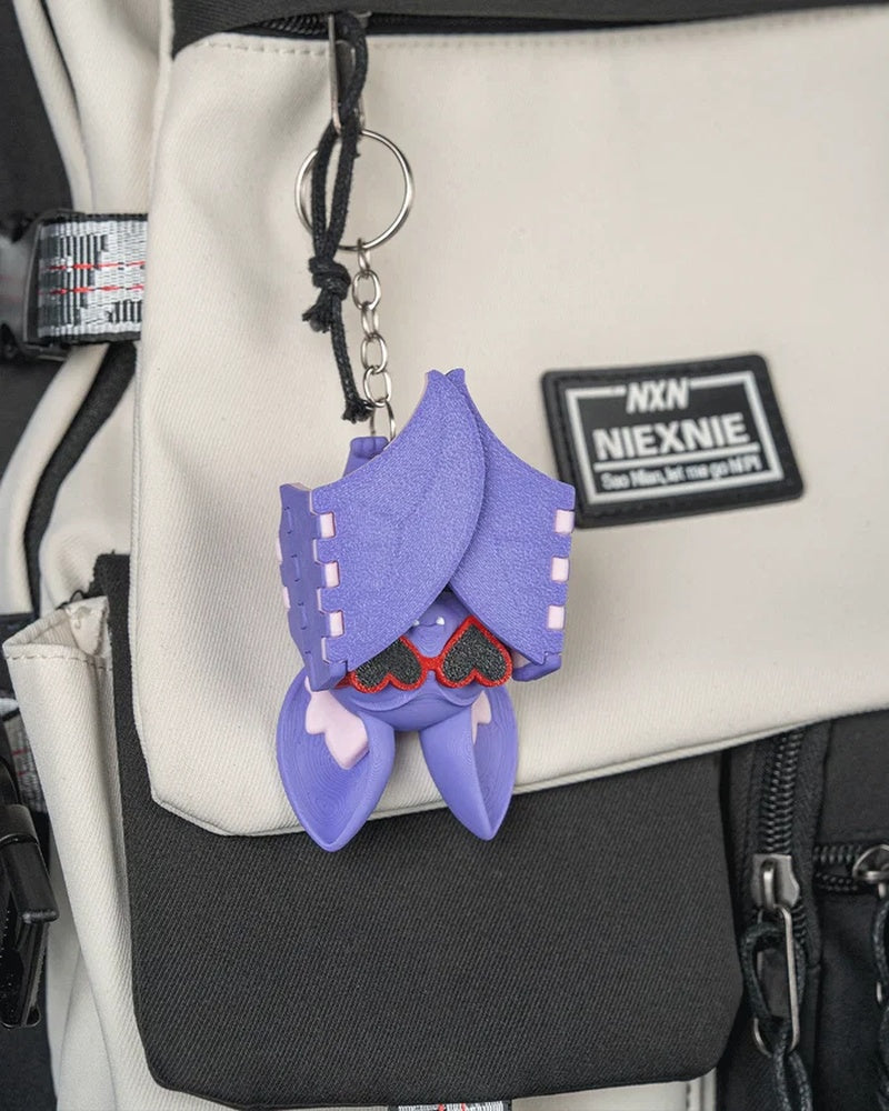 Purple bat figure hanging from a metal ring and chain on a light-colored bag