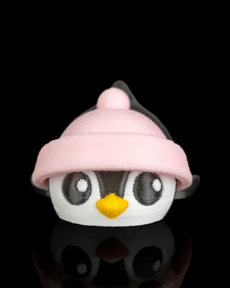 Front view of a penguin figurine with a pink hat, yellow beak, and round eyes on a black reflective surface.