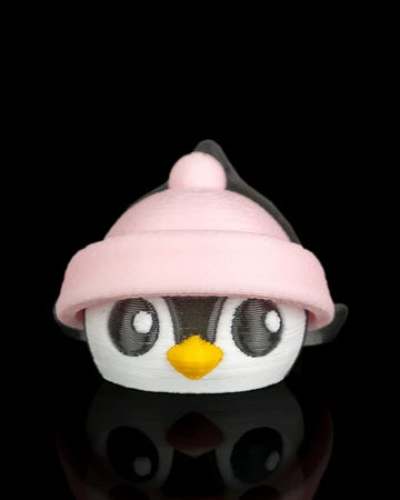 Front view of a penguin figurine with a pink hat, yellow beak, and round eyes on a black reflective surface.