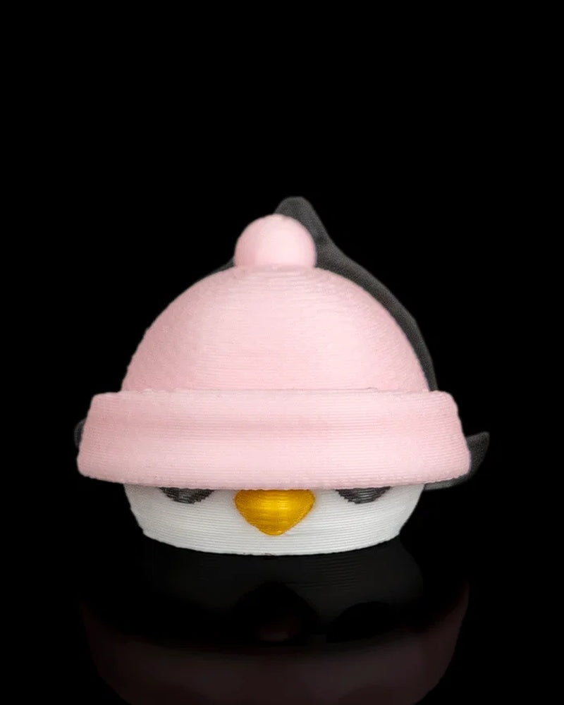Front view of a penguin figurine with a pink hat pulled low over its eyes on a black reflective surface.