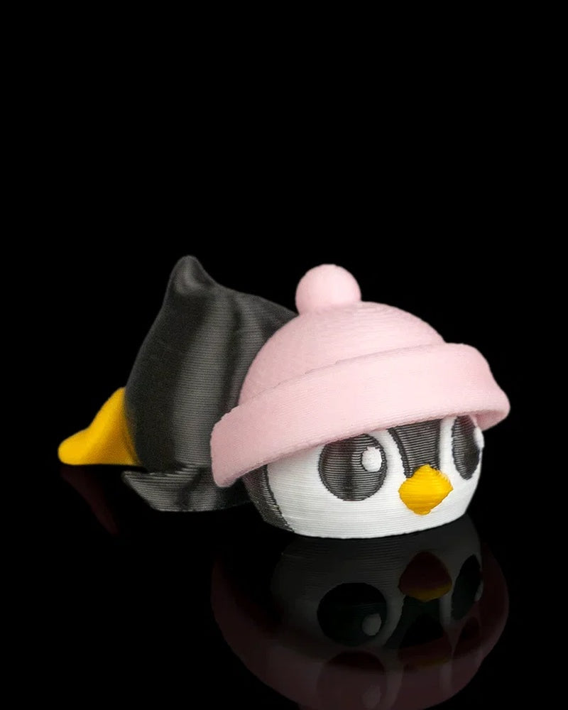 Angled view of a penguin figurine with a pink hat, yellow beak, black body, and yellow feet on a black reflective surface.