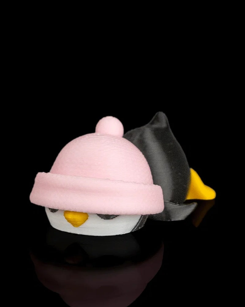 Side angled view of a penguin figurine with a pink hat, yellow beak, black body, and yellow feet on a black reflective surface.