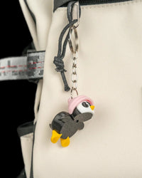 Small penguin figure hanging from a metal chain on a light-colored bag.