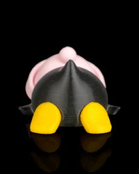 Rear view of a penguin figurine with a black body, pink hat, and yellow feet on a black reflective surface.