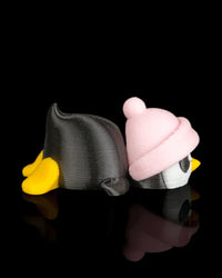 Side view of a penguin figurine with a black body, pink hat, white face, and yellow feet on a black reflective surface.