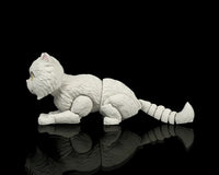 Side view of a low crouching white cat figurine with a raised tail on a black reflective surface