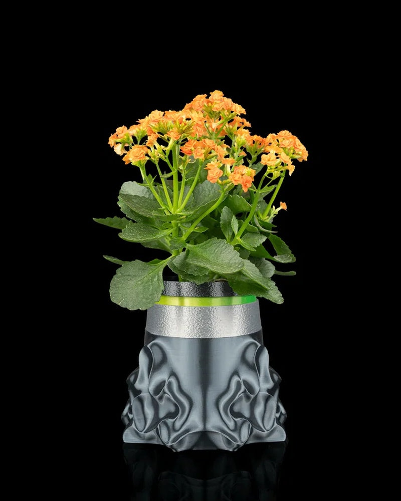 Gray sculptural planter holding a green plant with orange flowers on a black background