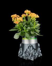Gray sculptural planter with a green plant and orange flowers viewed from the front