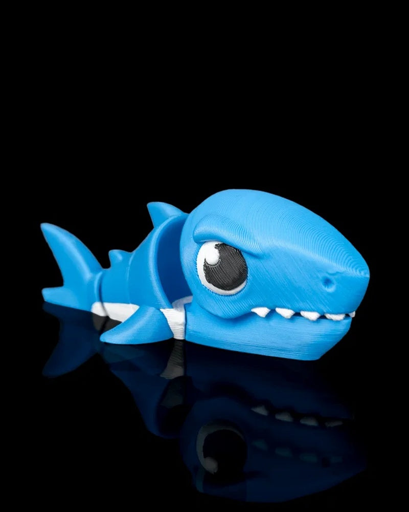Blue shark toy with white accents, teeth, fins, and tail on a black reflective surface