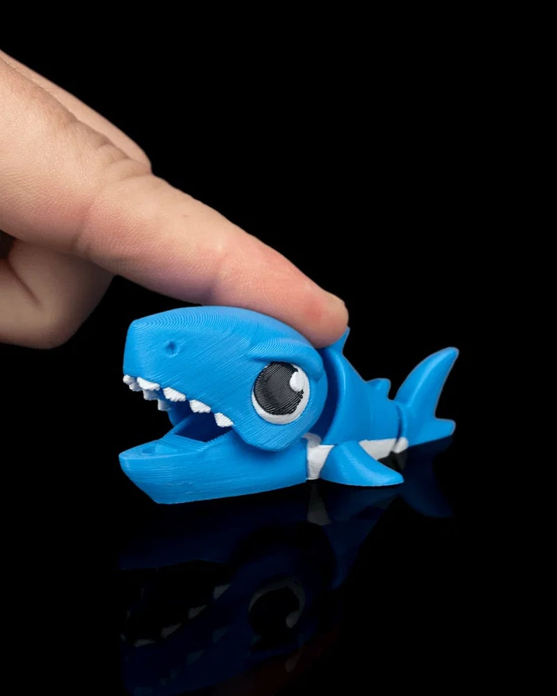 Blue shark toy with open mouth being pressed by a finger on a black background
