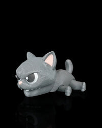 Gray cat snap toy with large eyes, pink nose, raised ears, and curled tail on a black surface