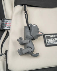 Gray cat toy hanging from a ring and cord on a beige bag