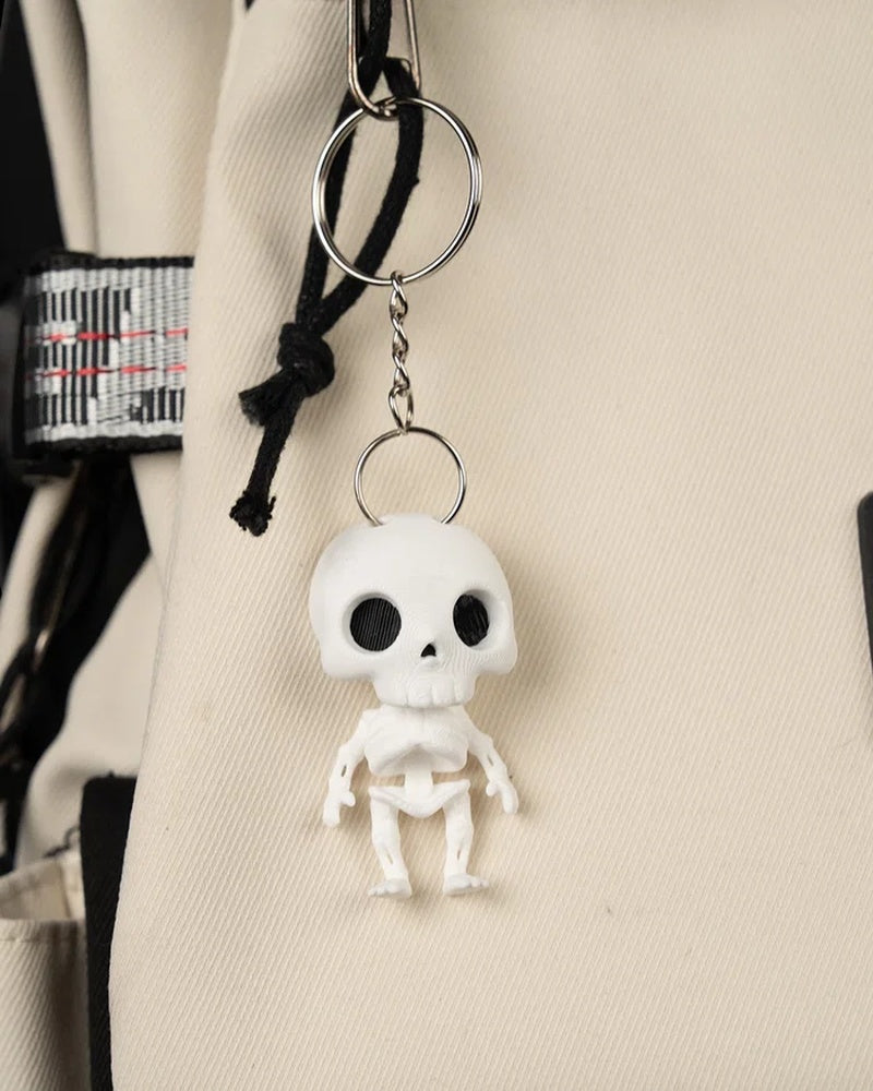 Small white skeleton figure hanging from a metal ring and chain against beige fabric