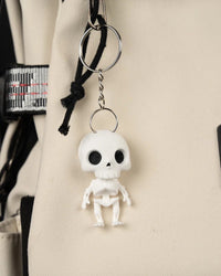 Small white skeleton figure hanging from a metal ring and chain against beige fabric