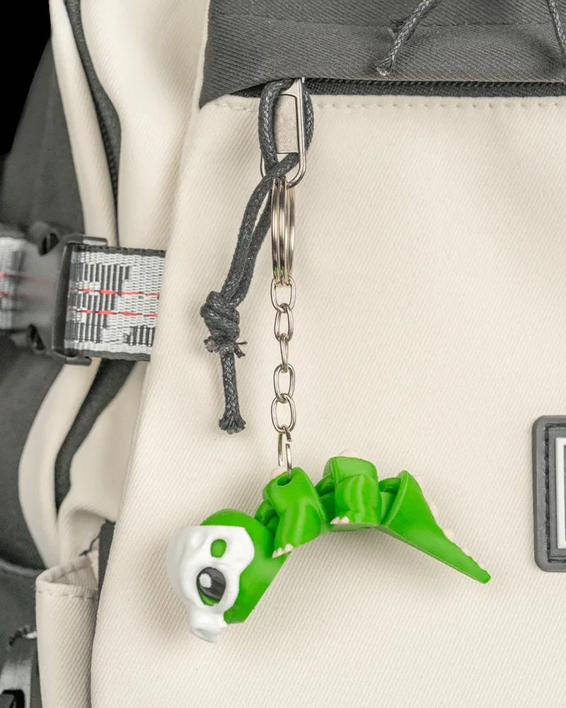 Green dinosaur figure hanging from a metal ring and chain on a backpack