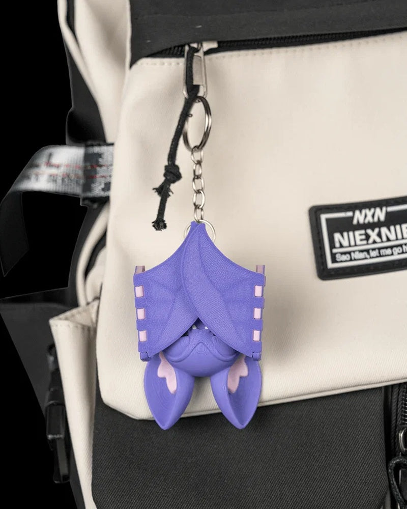 Purple bat hanging from a metal ring and chain on a beige and black bag