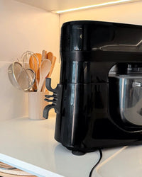 Gray cord holder attached to the side of a black countertop appliance in a kitchen