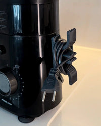 Gray cord holder with a coiled black appliance cord beside a black kitchen appliance