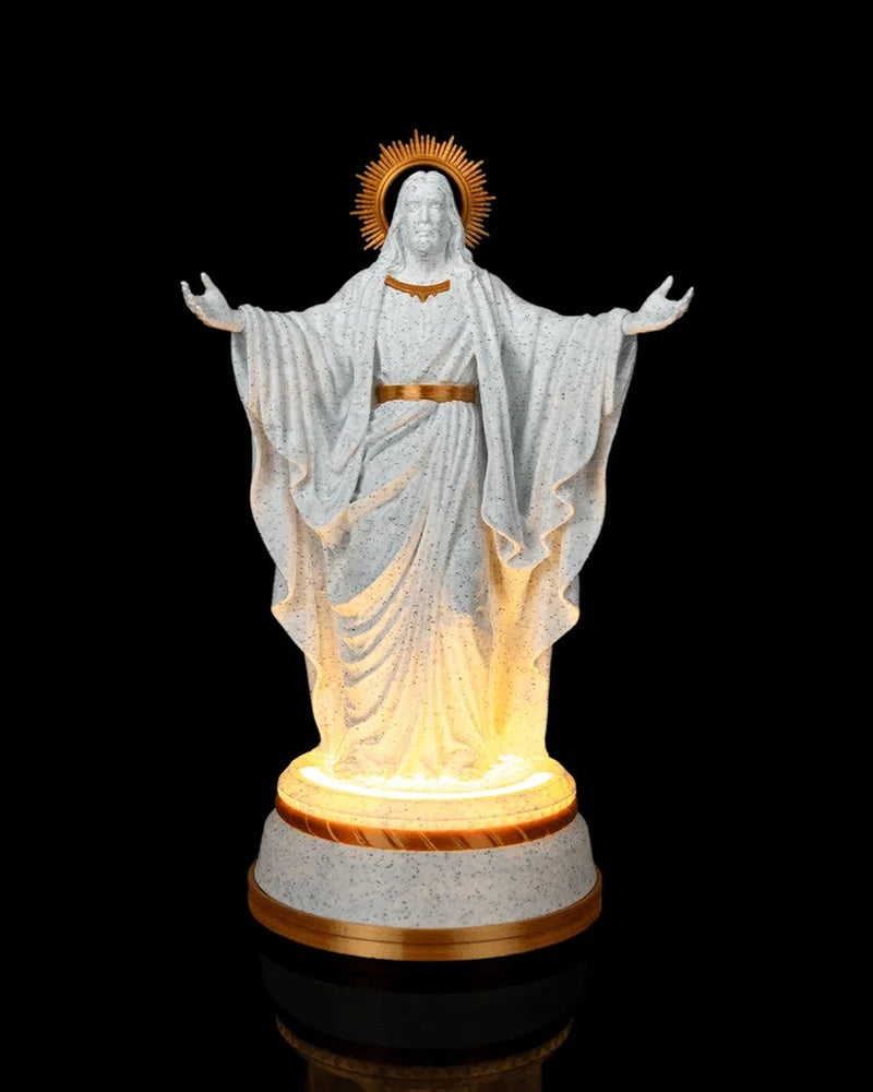 White and gold Christ statue with outstretched arms on a glowing round base against a black background