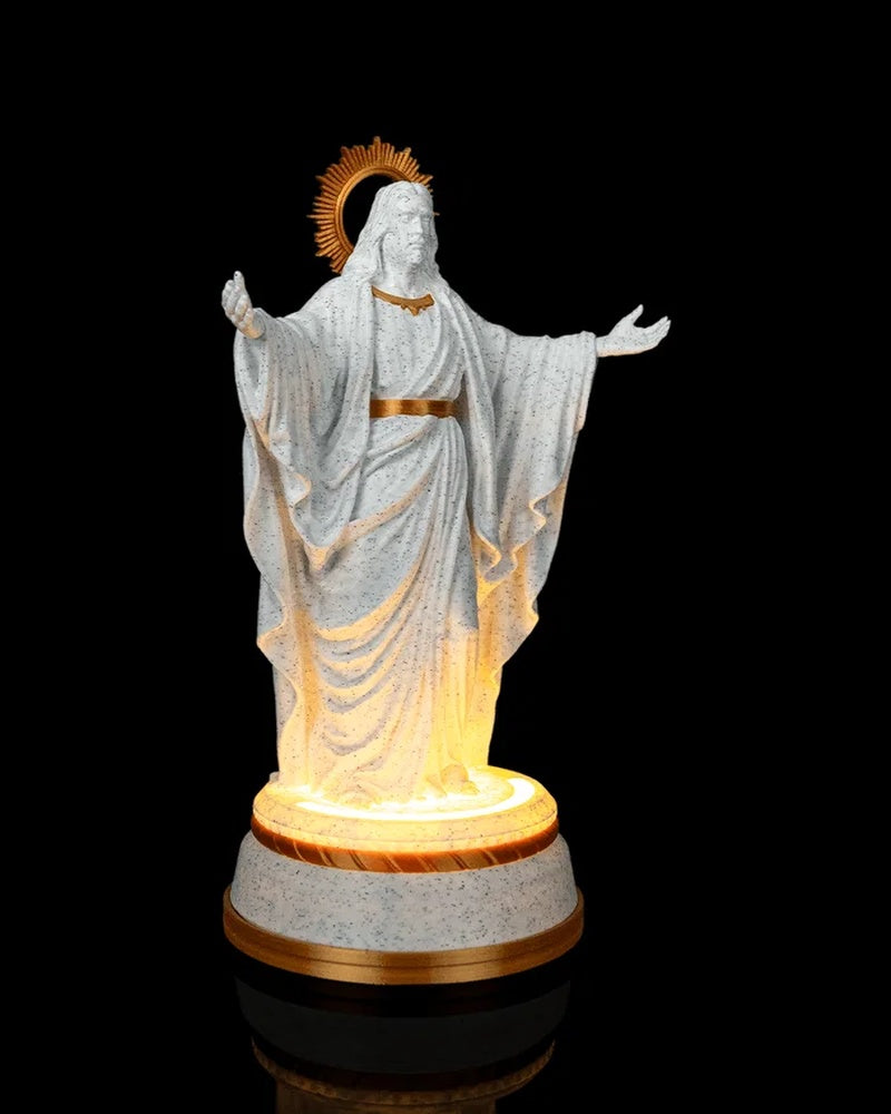 Angled front view of a white and gold Christ statue with outstretched arms and a glowing base