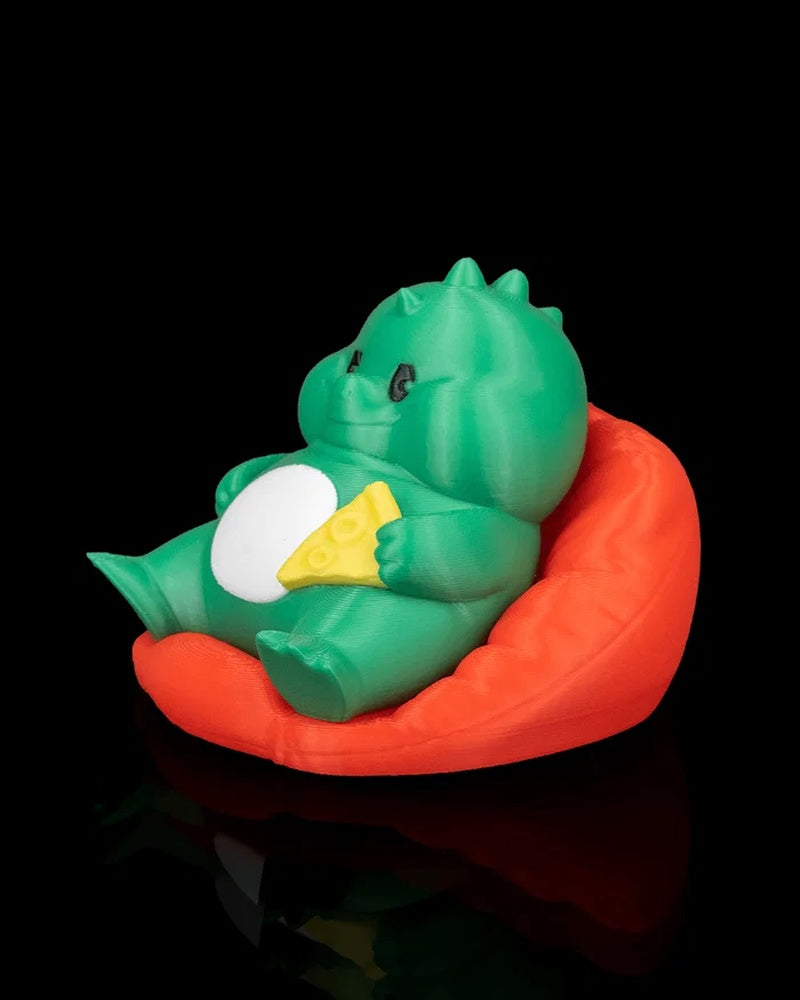 Side front view of a green dinosaur figurine seated in a red chair with a white belly and yellow snack detail