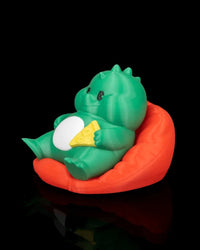 Side front view of a green dinosaur figurine seated in a red chair with a white belly and yellow snack detail