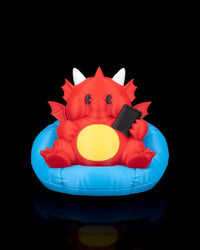 Front view of a red dragon figurine with white horns, yellow belly, small wings, and blue cushion on a black background.