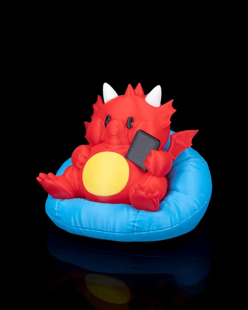 Angled front view of a red dragon figurine seated in a blue cushion and holding a small black rectangle.