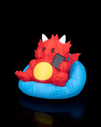 Angled front view of a red dragon figurine seated in a blue cushion and holding a small black rectangle.