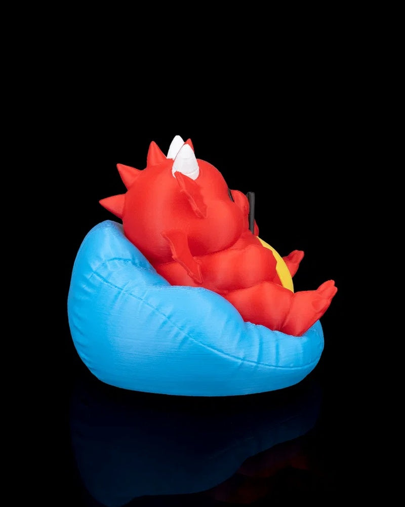 Side view of a red dragon figurine reclining in a blue cushion with white horns visible against a black background.