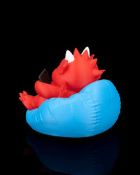 Rear angled view of a red dragon figurine in a blue cushion with spikes, wings, and a small black rectangle visible.