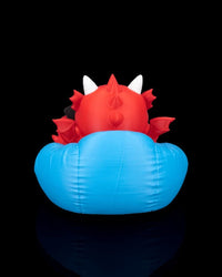 Back view of a red dragon figurine seated in a blue cushion with white horns, small wings, and back spikes.