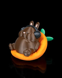 Angled front view of a brown rabbit figurine with black headphones in an orange carrot-shaped seat with green leaves.