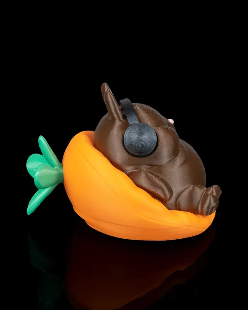 Side view of a brown rabbit figurine wearing black headphones in an orange carrot-shaped seat with green leaves.