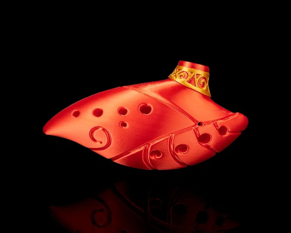 Red ocarina-shaped figurine with round holes, raised swirl details, and a gold-toned collar on a black background