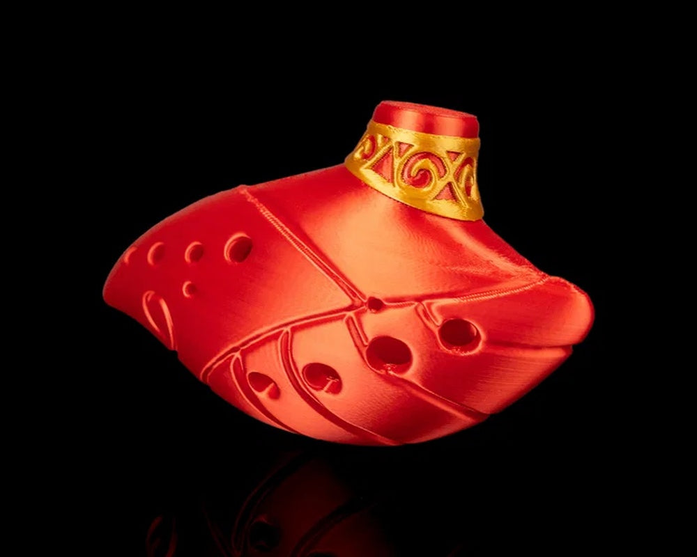 Angled view of a red ocarina-shaped figurine with multiple round openings and a gold-toned patterned collar