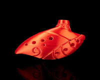 Red ocarina-shaped figurine with round holes, curved body, swirl accents, and gold-toned top detail