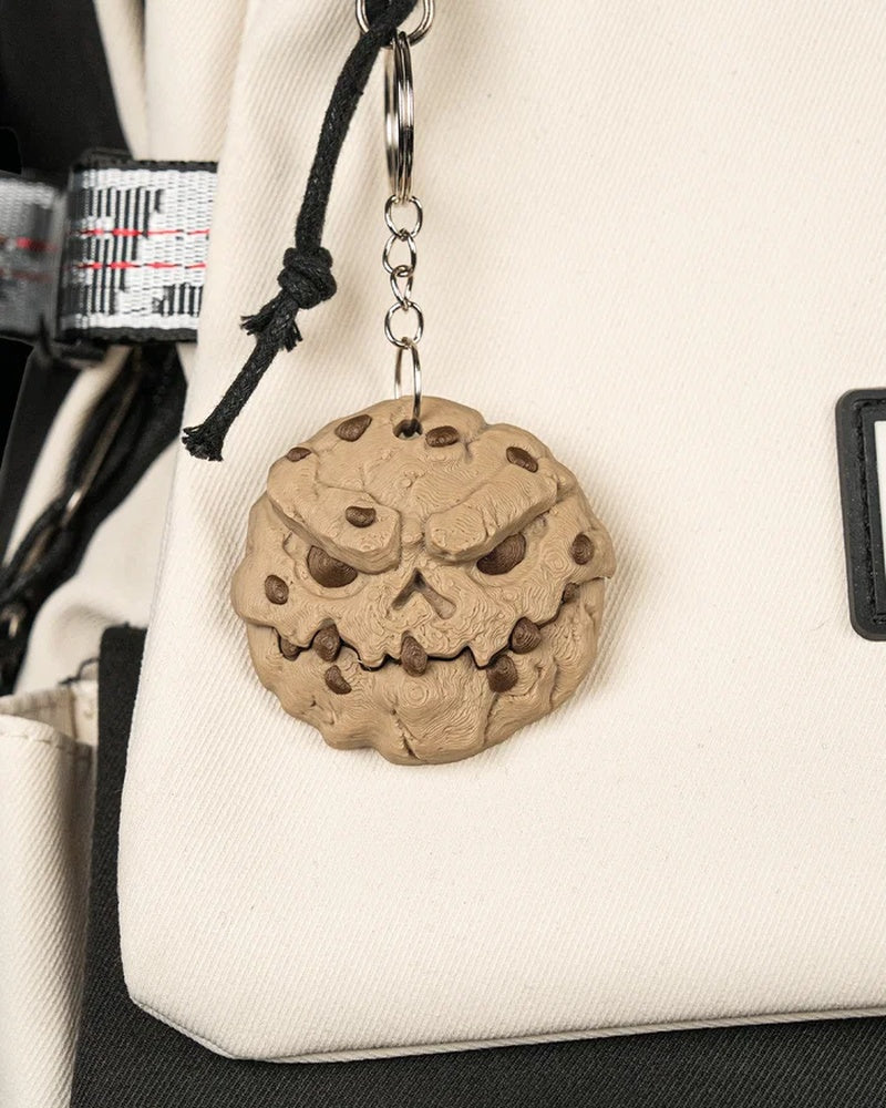 Tan round monster face with brown spots hanging from metal rings against a cream bag.