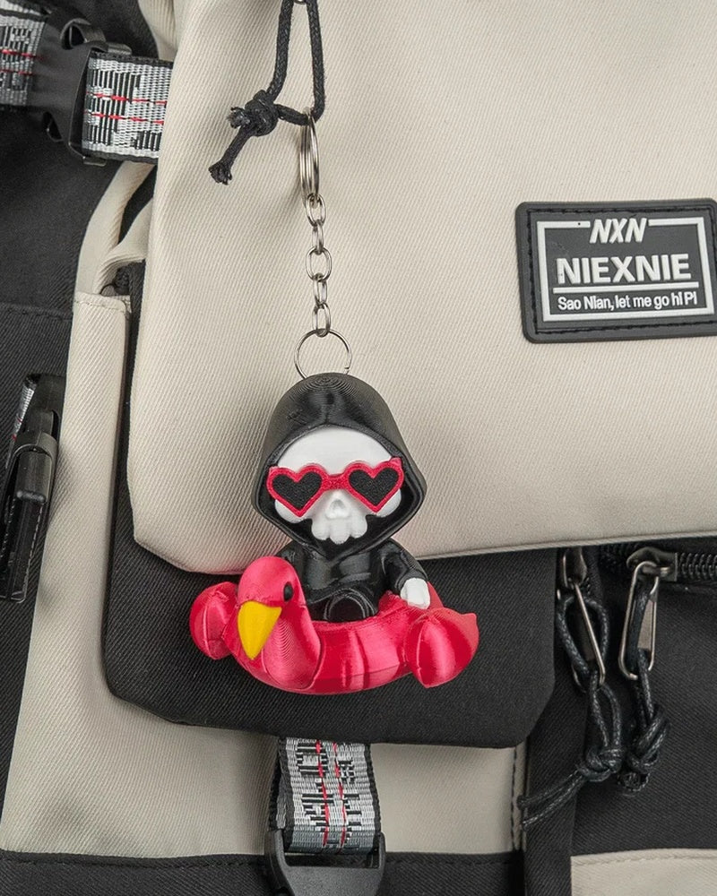 Small hooded skull character in a pink flamingo float hanging by a ring and chain from a backpack
