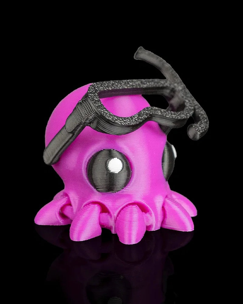 Side-front view of a bright pink octopus figure with black goggles and tentacles on a black background.