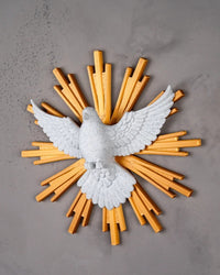 Angled view of a white dove figurine with spread wings and golden rays on a gray wall