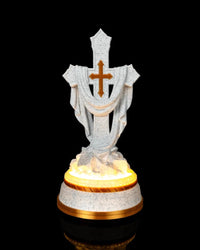 Front view of a white speckled draped cross statue with a gold-tone cross accent and glowing base on a black background.