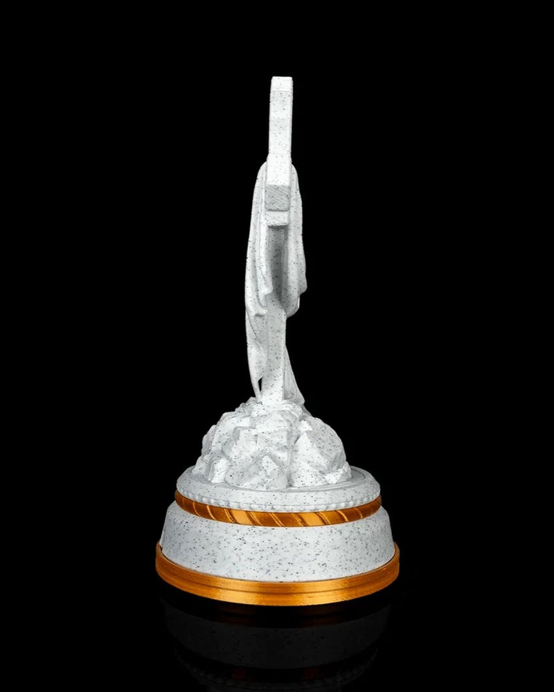 Side view of a white speckled draped cross statue on a tiered base with gold-tone trim.