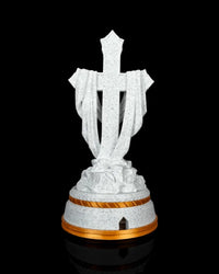 Back view of a white speckled draped cross statue on a tiered base with gold-tone trim and a small rear opening.