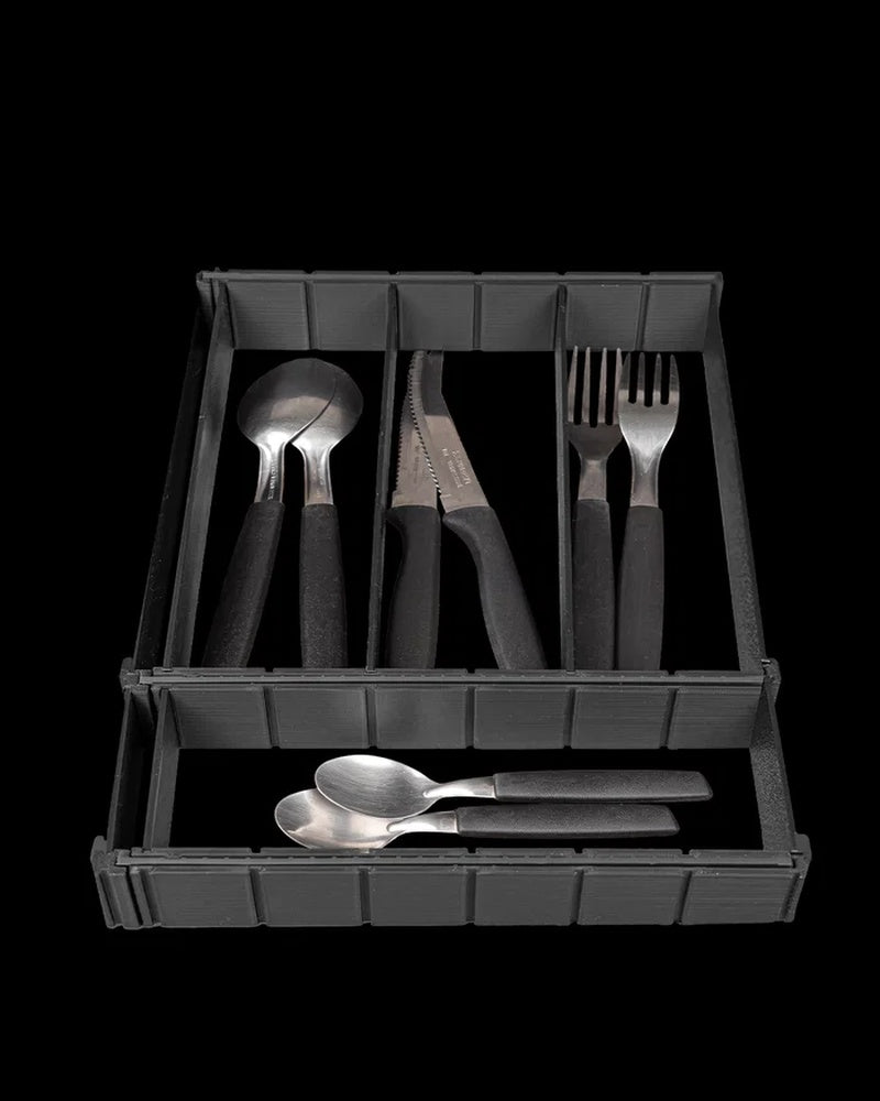 Black partitioned drawer organizer holding spoons, knives, and forks on a dark background