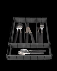 Black partitioned drawer organizer holding spoons, knives, and forks on a dark background